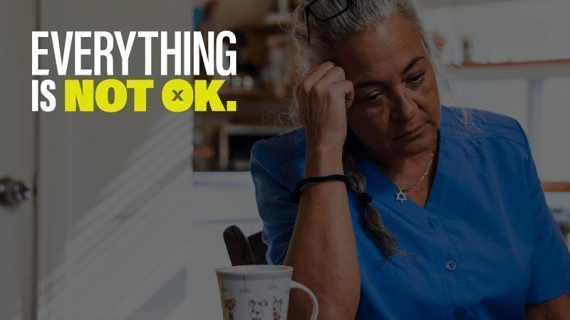 Older white woman sitting at table looking upset with the words Everything is Not Ok